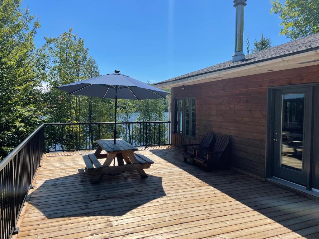 eine Holzterrasse mit einem Picknicktisch und einem Sonnenschirm in der Unterkunft Les Chalets du Lac Grenier in Chertsey