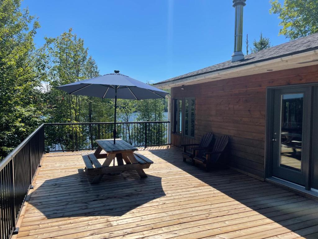 una terraza de madera con mesa de picnic y sombrilla en Les Chalets du Lac Grenier, en Chertsey