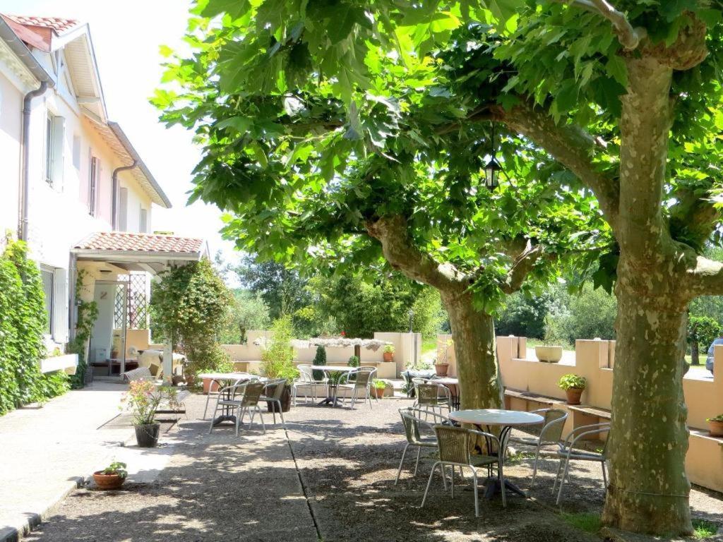 um pátio com mesas e cadeiras debaixo de uma árvore em Logis Hôtel Le Clos Pité em Préchacq