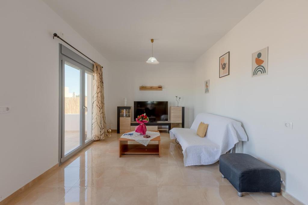 a white living room with a couch and a tv at House on the black beach with sea view and parking in Agios Georgios Thalassiti