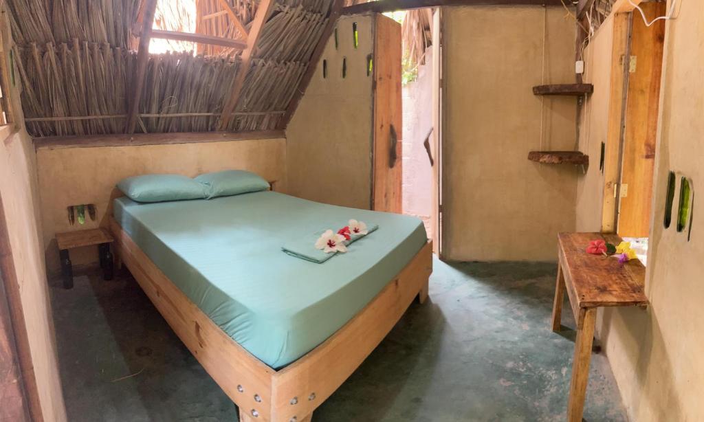 Una cama en una habitación con dos flores. en La Aldea Hostel, Camping y Hamacas en Palomino