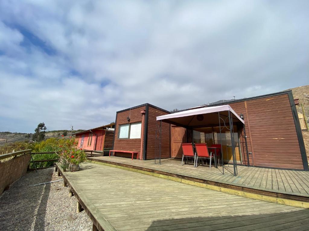 a house with a deck with chairs and an umbrella at Cabaña Girasol - Cocina Parking Piscina Wifi in Algarrobito