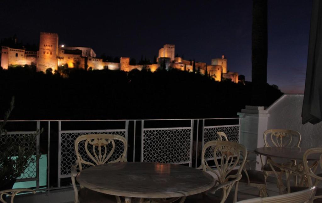 a table and chairs on a balcony with a castle at night at Suite Comares in Granada