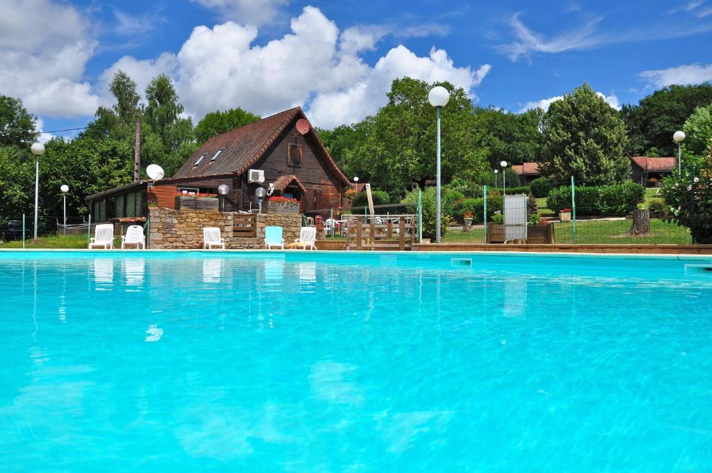ein großer Pool mit einem Gebäude im Hintergrund in der Unterkunft Les Chalets de Thegra proche de Rocamadour et Padirac in Thégra
