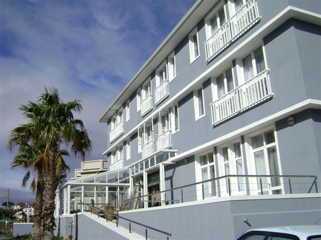 een blauw gebouw met witte balkons en een palmboom bij The Calders Hotel & Conference Centre in Fish hoek