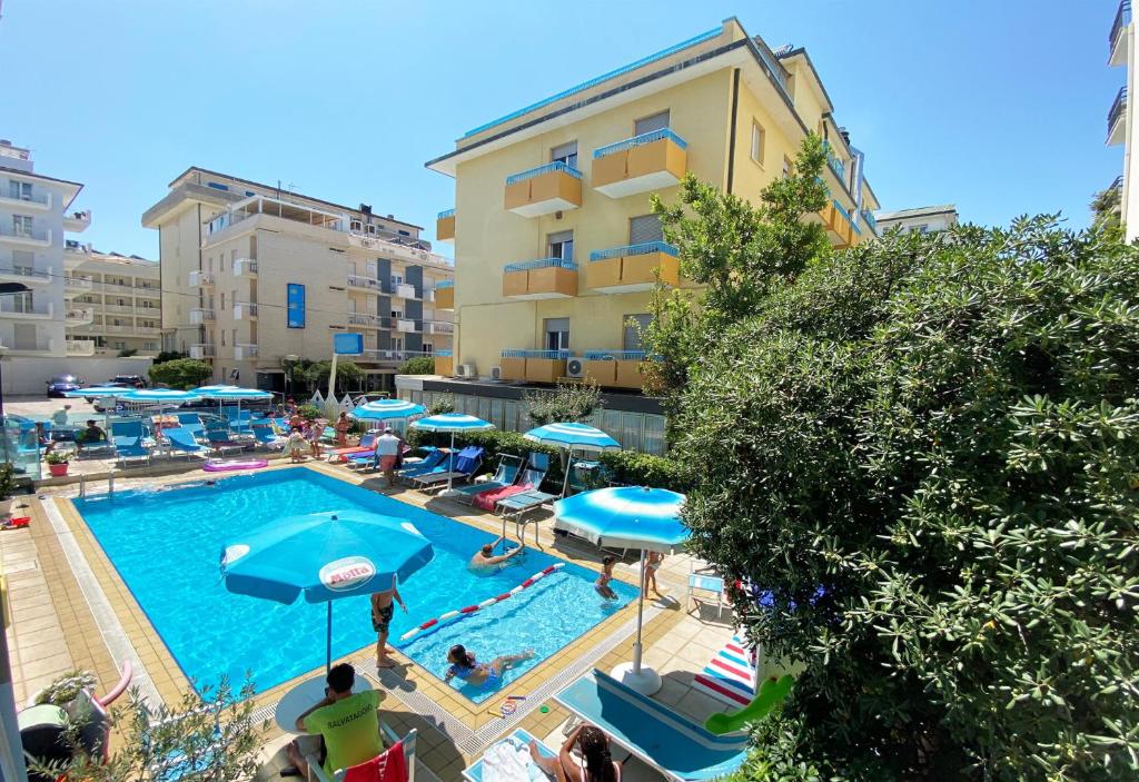 una piscina con sombrillas azules y un edificio en Hotel Adelphi, en Riccione