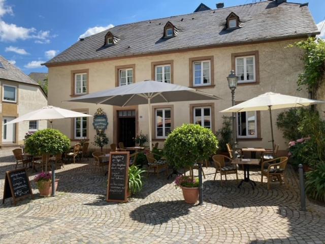 ein Restaurant mit Tischen und Sonnenschirmen vor einem Gebäude in der Unterkunft Warsberger Weinhof - Hotel & Weinwirtschaft in Neumagen-Dhron