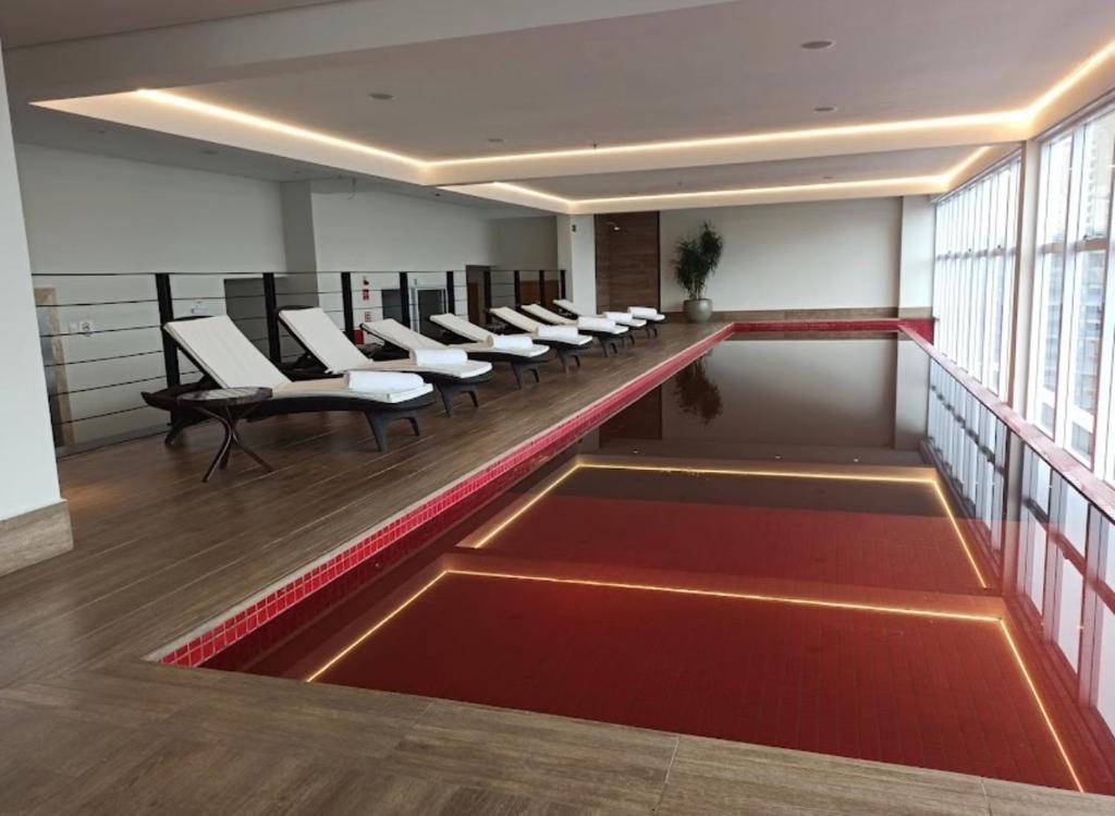 una sala de espera con sillas blancas y suelo rojo en QS Marista - Studio Alessandra Antonelli - Flat 1708 en Goiânia