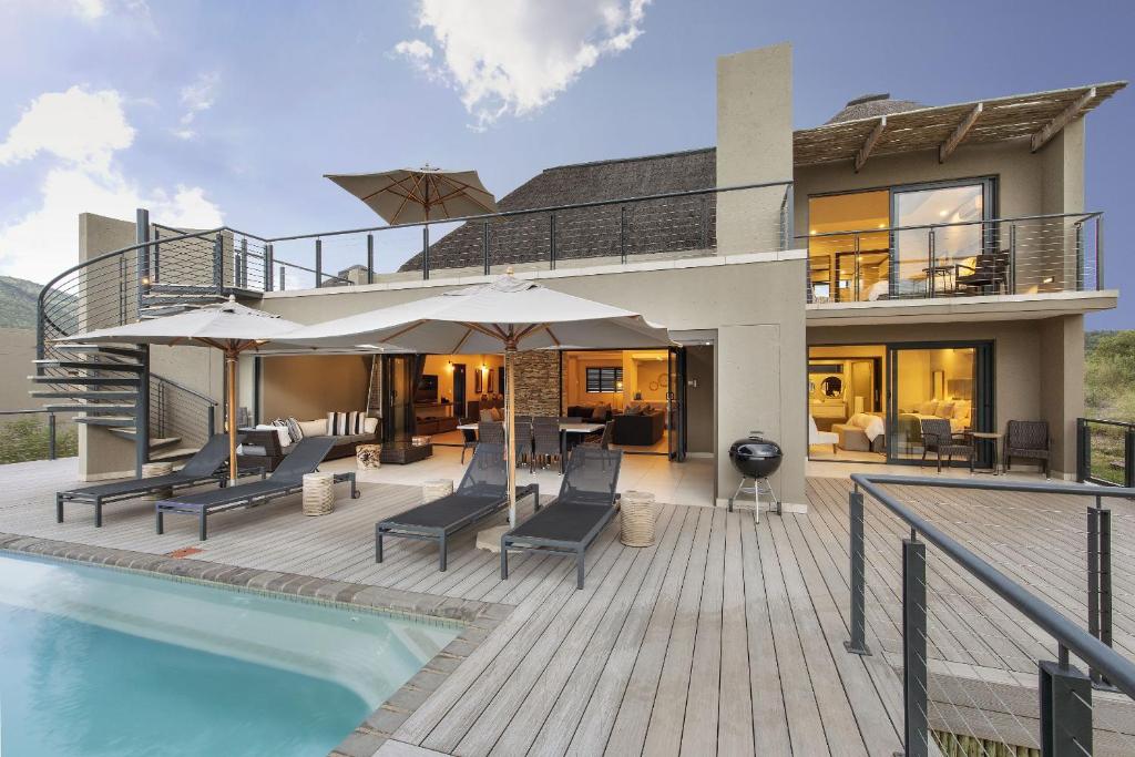 a house with a pool and a deck with chairs and umbrellas at Bakubung Villas in Pilanesberg