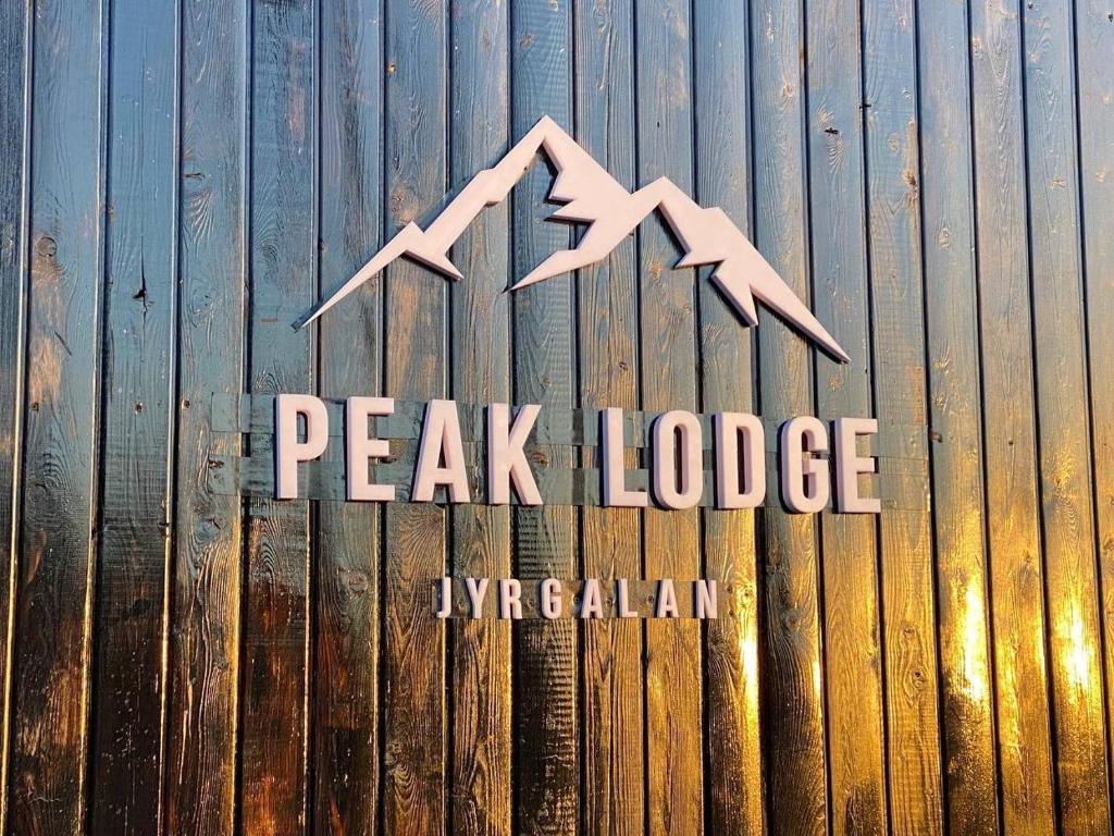 a sign for a peak lodge on a wooden fence at Peak Lodge Jyrgalan in Dzhergalan