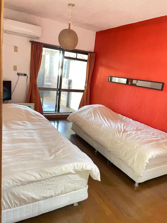 um quarto com 2 camas e uma parede vermelha em ゲストハウス303 em Zamami