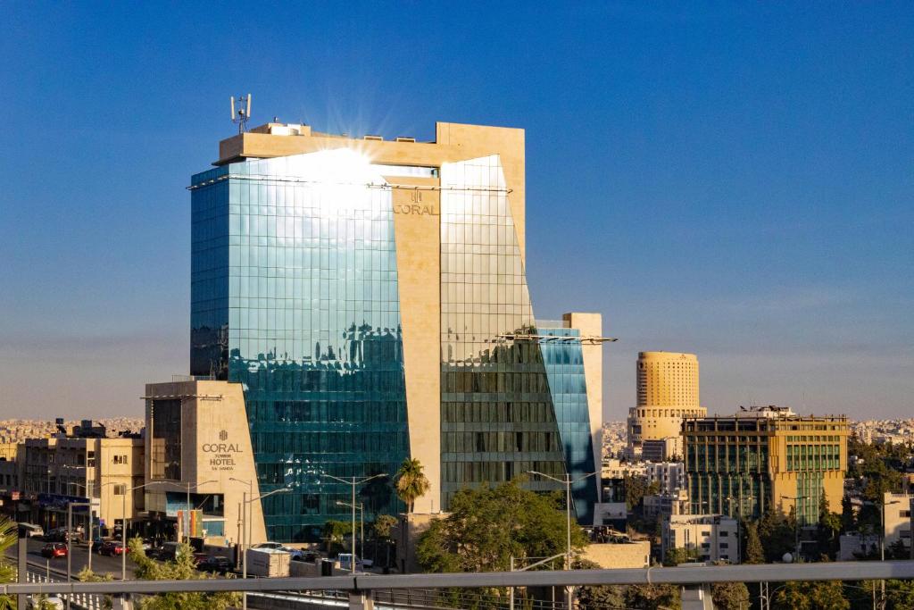 wysoki szklany budynek przed miastem w obiekcie Coral Tower Hotel by Hansa w mieście Amman