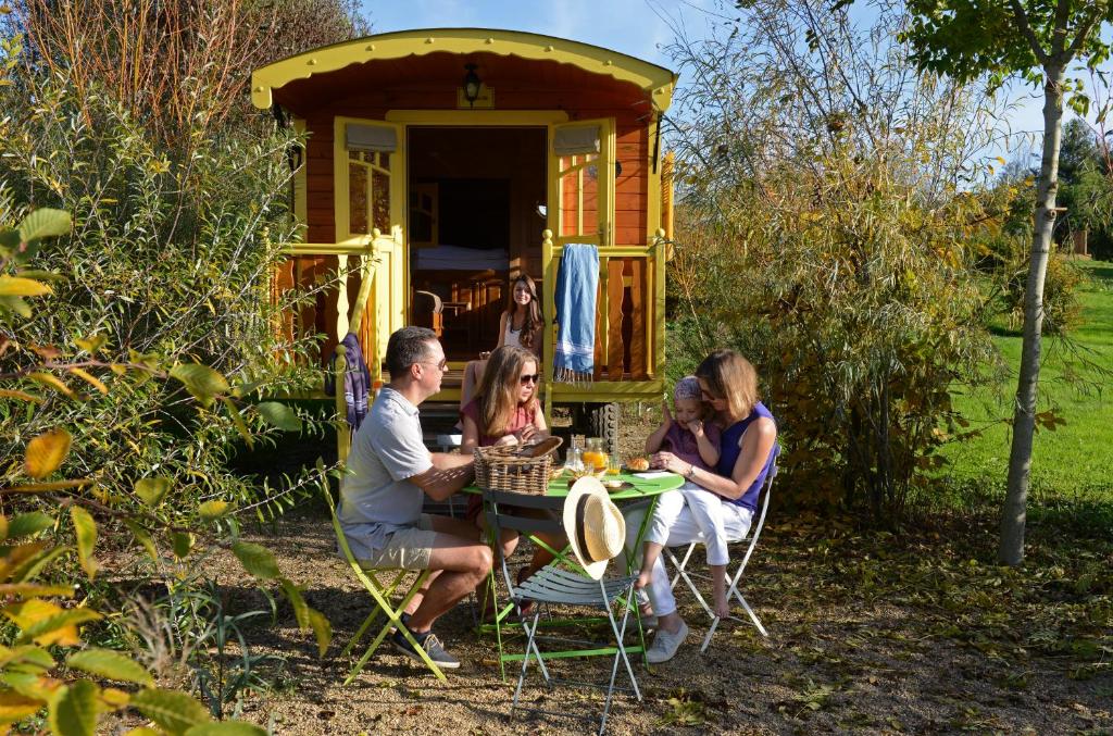 Un gruppo di persone sedute a un tavolo di fronte a una casetta di Les Roulottes & Cottages du Moulin a Chenillé-Changé