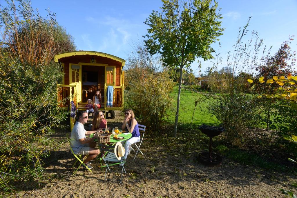 a group of people sitting at a table in front of a house at Les Roulottes & Cottages du Moulin in Chenillé-Changé