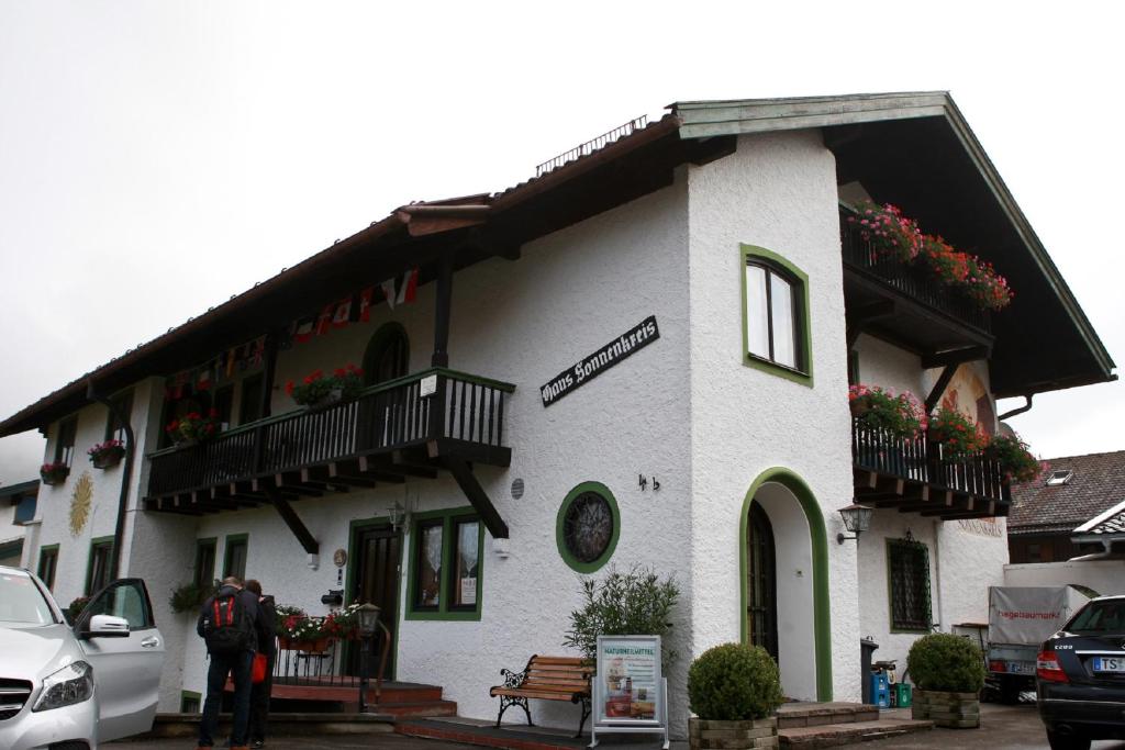 a white building with balconies and a man standing outside at Ferienwohnungen Gästehaus Sonnenkreis in Ruhpolding