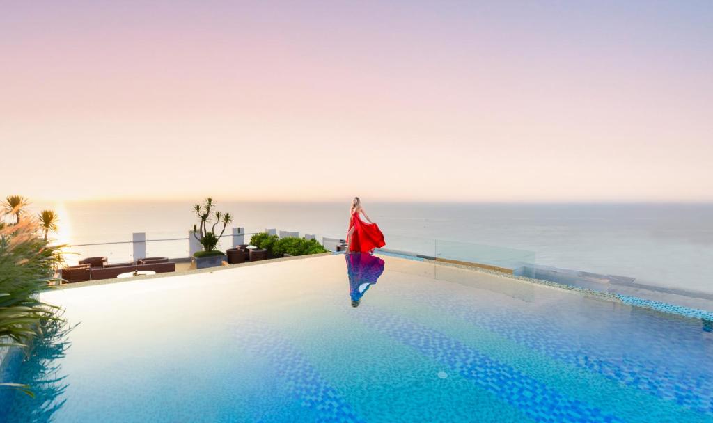 a person standing on the edge of a swimming pool overlooking the ocean at HAIAN Beach Hotel & Spa in Danang