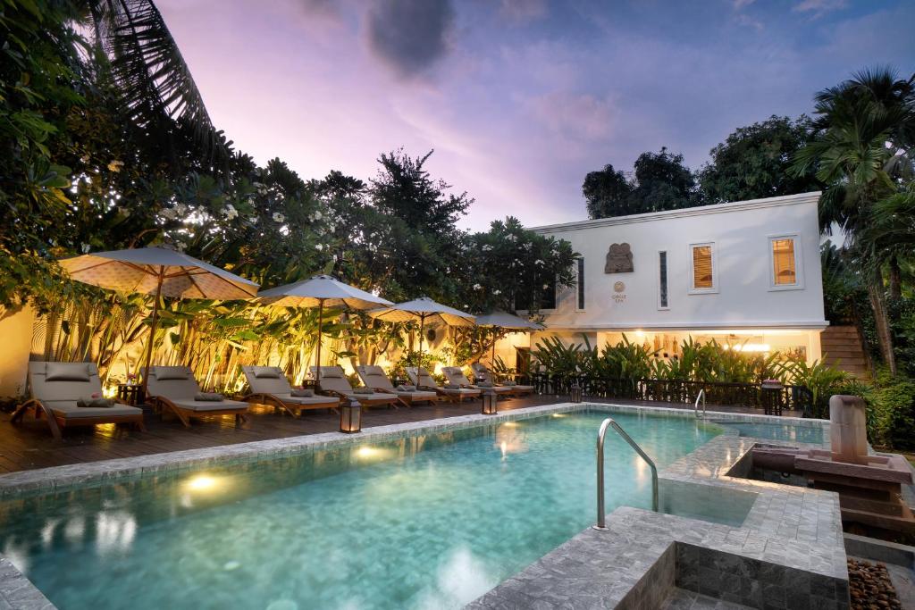 a resort pool with lounge chairs and umbrellas at night at Mane History Lovers in Siem Reap