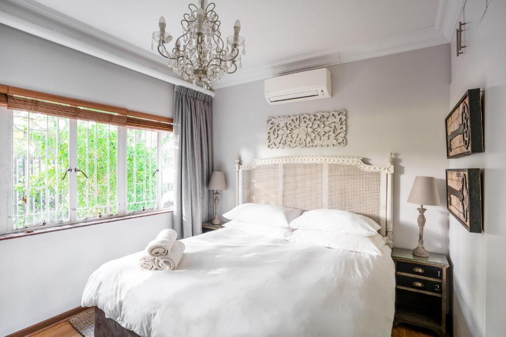 a white bedroom with a bed with white sheets and a chandelier at Avemore Wag n Bietjie No 1 in Stellenbosch