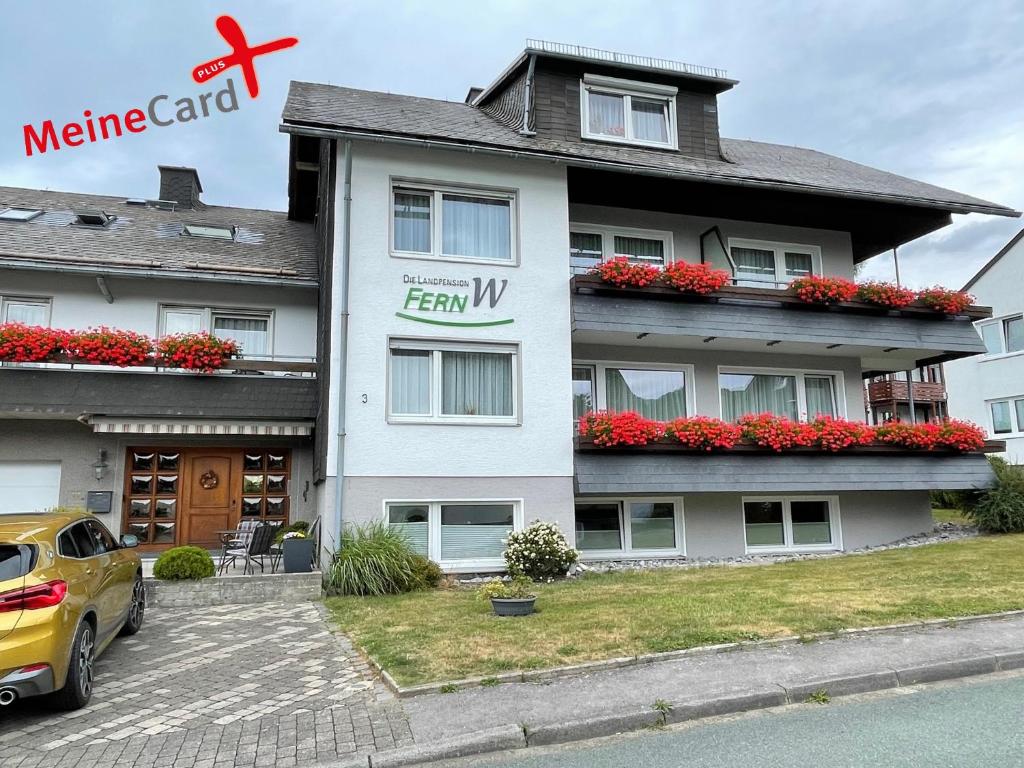 Un grand bâtiment blanc avec des fleurs rouges sur les balcons dans l'établissement Die Landpension FernW, à Willingen