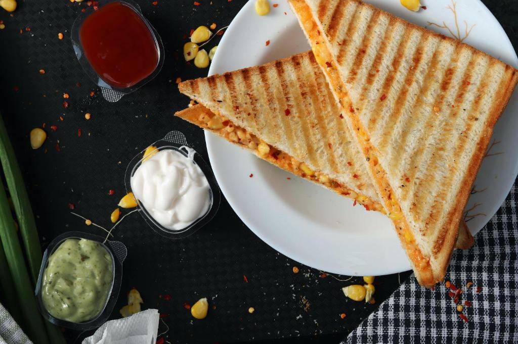 un plato blanco con dos sándwiches de queso a la parrilla y salsas en Hotel Maya 'NEW DELHI', en Nueva Delhi