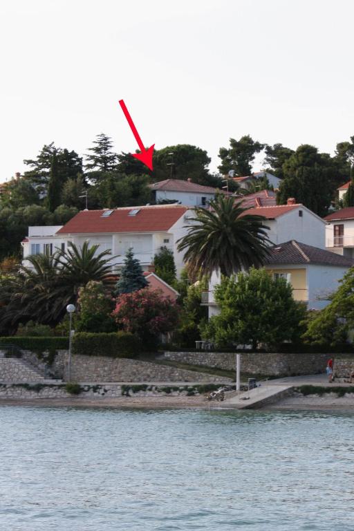 a house with a red butterfly on top of it next to the water at Double Room Banjol 5077b in Rab