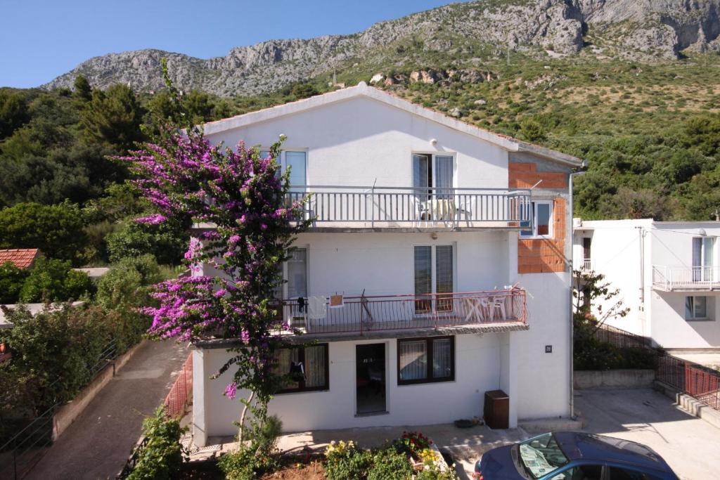 une maison blanche avec un arbre et des fleurs violettes dans l'établissement Studio Podaca 6745c, à Podaca