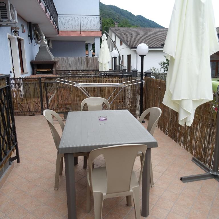 uma mesa e cadeiras num pátio com um guarda-sol em Appartamento ROSA - Colori del Lago d'Orta - NUOVA STRUTTURA A OMEGNA em Omegna