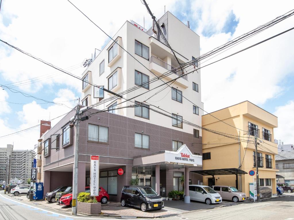 een hoog gebouw met auto's geparkeerd voor het bij Tabist Rays Hotel Yakata in Miyazaki