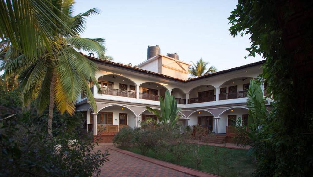 a large white building with a palm tree at Dunhill Beach Resort in Agonda