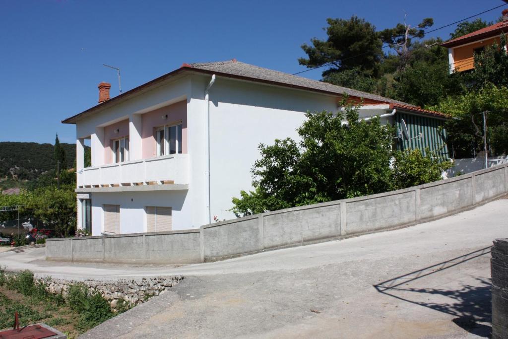 a white house next to a concrete wall at Apartments by the sea Supetarska Draga - Donja, Rab - 4981 in Supetarska Draga