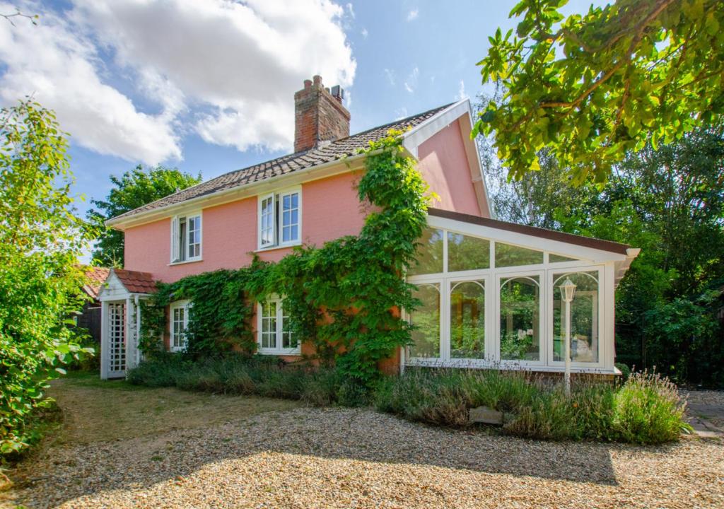 una casa rosa con un salón acristalado delante de ella en Barn Meadow Cottage, en Yoxford