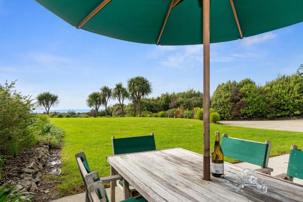 a picnic table with an umbrella and a bottle of wine at Sea View Cottage - Ruakaka Holiday Cottage in Ruakaka