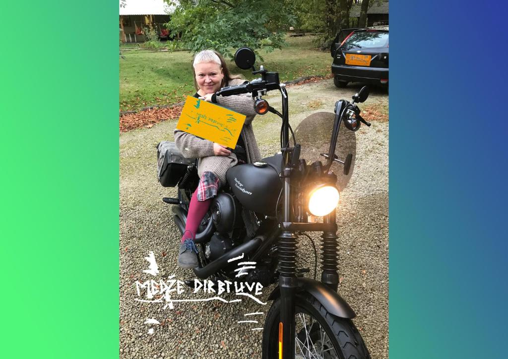 Eine Frau auf einem Motorrad mit einem Schild drauf. in der Unterkunft Medže dirbtuve 