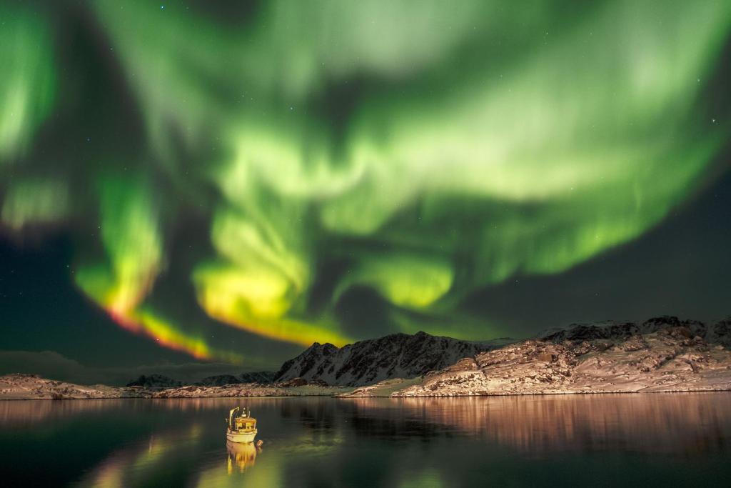 un barco en el agua bajo la aurora boreal en Utsikten en Gjesvær