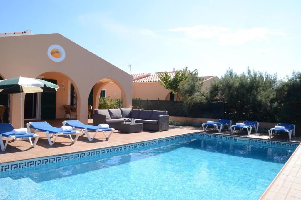 uma piscina com cadeiras e um guarda-sol ao lado de uma casa em Villas Las Golondrinas em Cala'n Bosch
