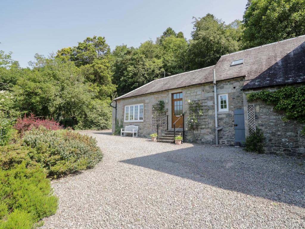 a stone house with a gravel driveway in front of it at Stables Cottage in Langholm