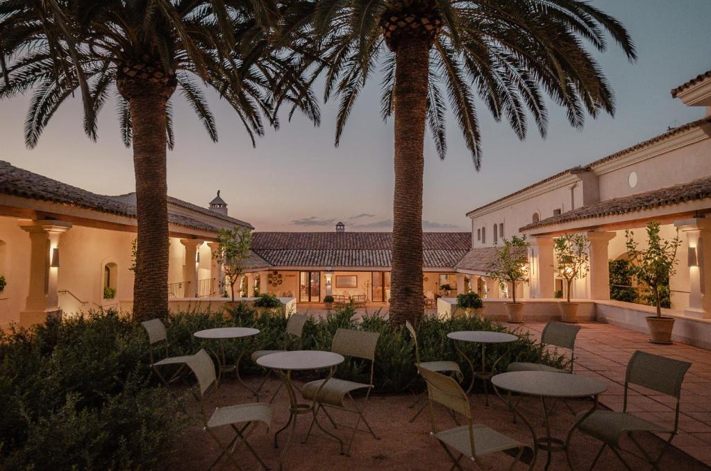 un patio con mesas, sillas y palmeras en La Dehesa de Don Pedro en Monesterio