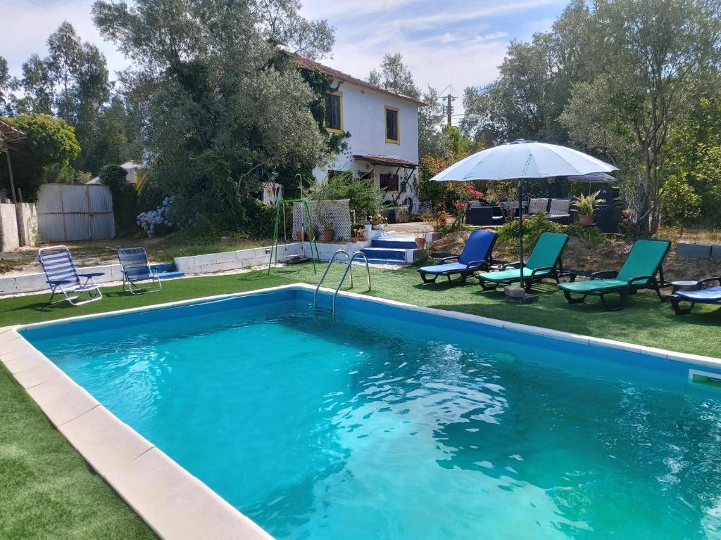 a swimming pool in a yard with chairs and an umbrella at A casinha in Vila Nova de Anços