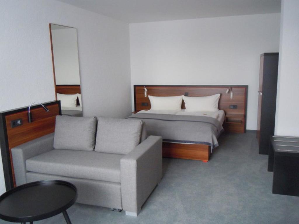 ein Schlafzimmer mit einem Bett, einem Sofa und einem Stuhl in der Unterkunft Allgäuhotel Memmingen Nord in Memmingen