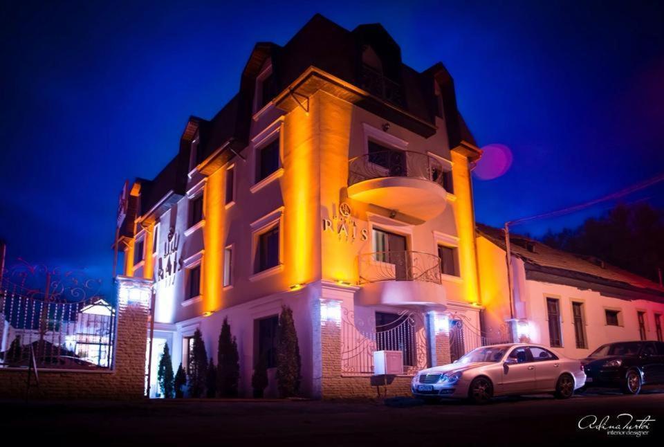 een witte auto geparkeerd voor een gebouw 's nachts bij Hotel Rais in Târgu Jiu