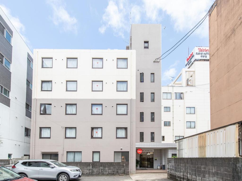 een wit gebouw met auto's ervoor geparkeerd bij Tabist Rays Hotel Suisen in Miyazaki