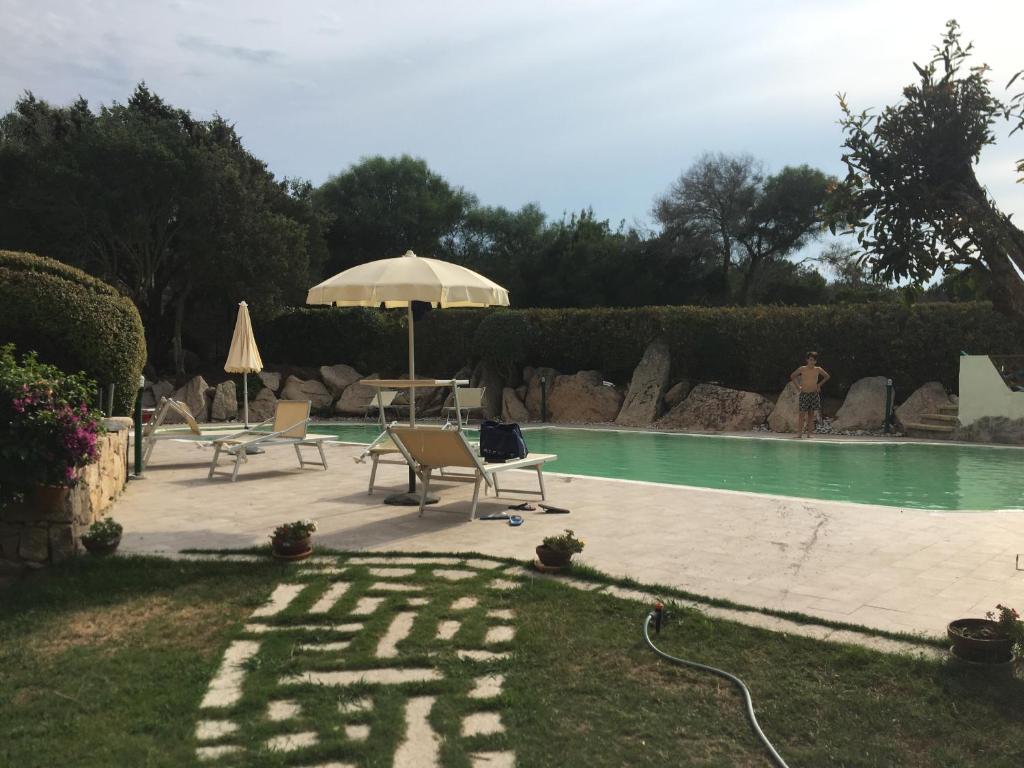 Abbiadori的住宿－green park cala di volpe，一个带遮阳伞和两把椅子及一张桌子的游泳池