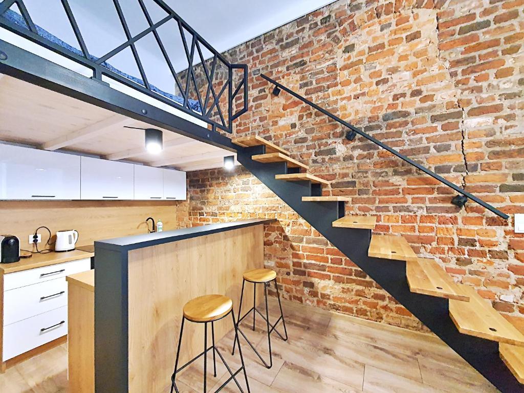 a brick wall with a staircase in a kitchen with stools at Apartamenty Dream Place in Toruń