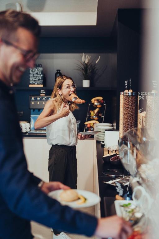 a woman standing in a kitchen with a man eating food at Airbase Hotel in Kalsdorf bei Graz