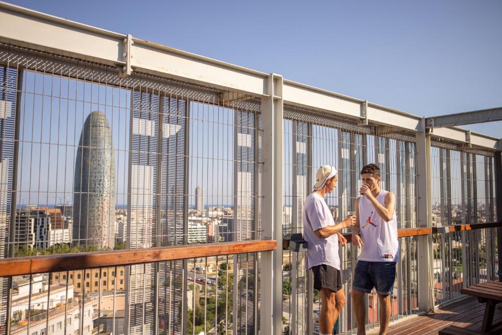 dos personas de pie en un balcón con vistas a una ciudad en Urbany Hostel Barcelona, en Barcelona