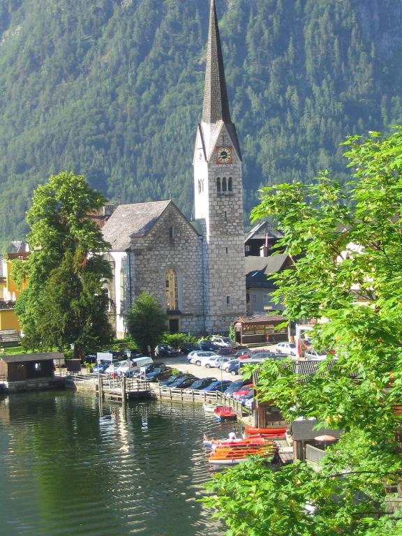 a church with a steeple and boats in the water at Pension Sarstein in Hallstatt