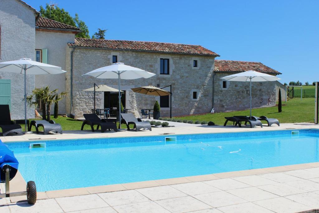 - une piscine en face d'une maison avec des parasols dans l'établissement Aux Vents d'anges, à Cahuzac-sur-Vère