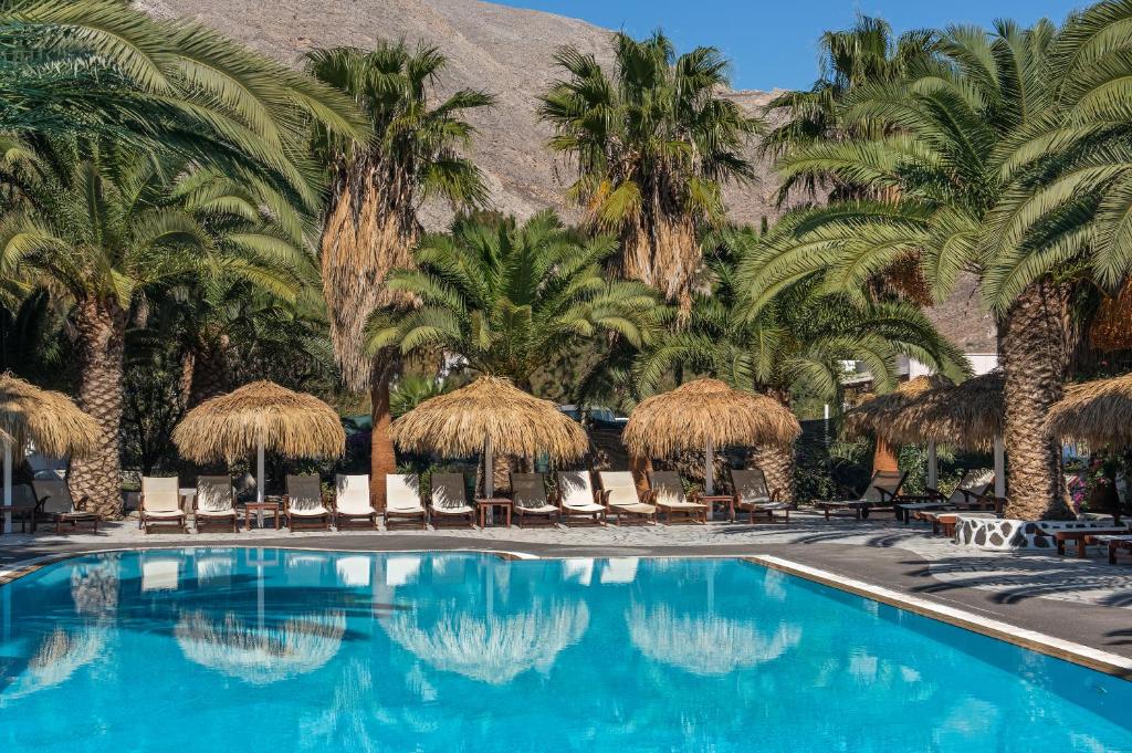 - une piscine bordée de palmiers et de parasols dans l'établissement Meltemi Village Hotel, à Perissa