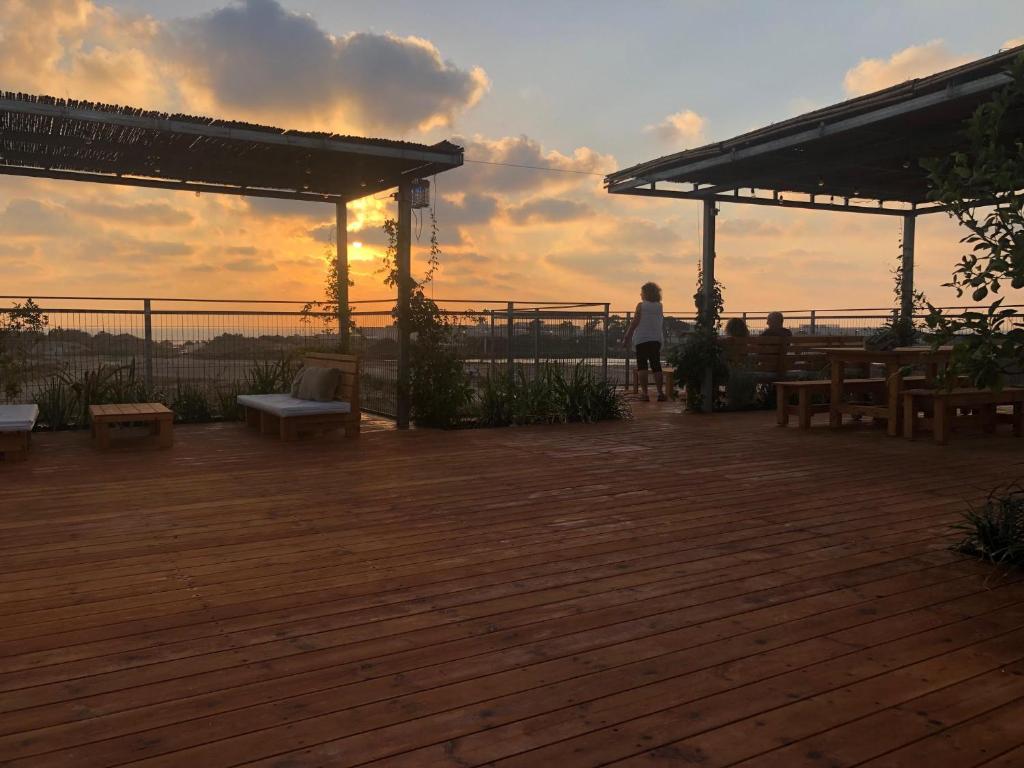 a woman standing on a deck with a sunset in the background at Atlit Rooftop Glamping in Atlit