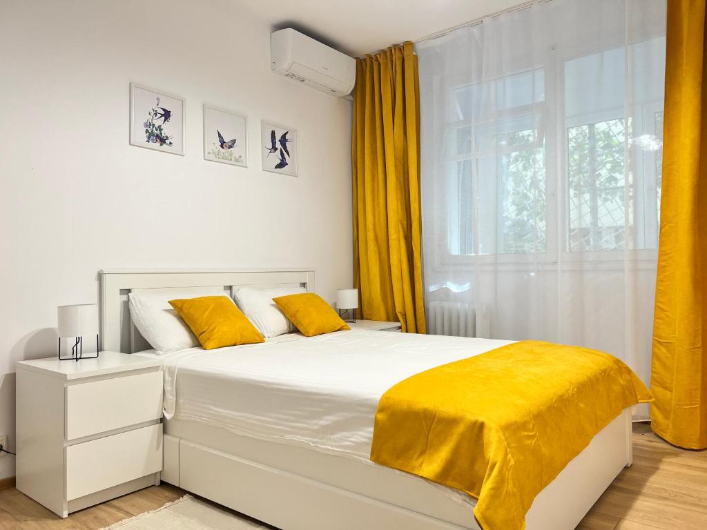 a bedroom with a white bed with yellow sheets and a window at RSA apartment - Comfort near City Centre in Bucharest